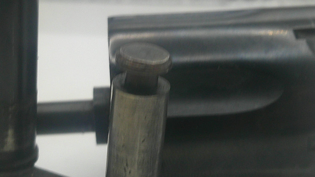 Close-up of a dark metal cylindrical component with a round metallic cap or knob, set against a mostly dark and light gray background.