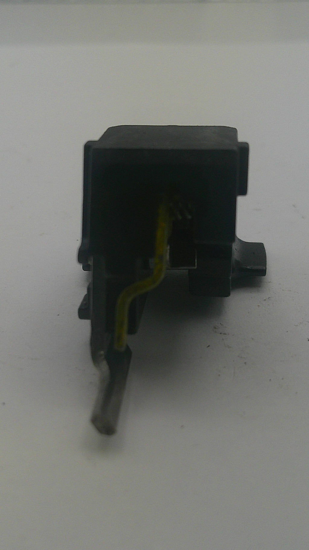 A small black plastic electronic component or switch with a yellow wire attached, photographed against a plain off-white background.