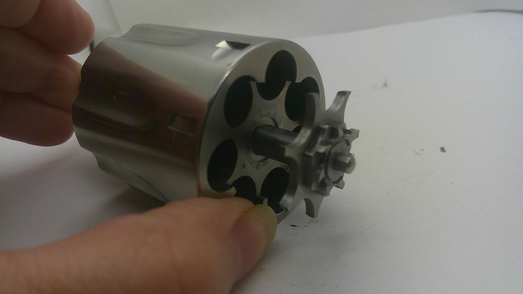 A close-up of a metallic revolver cylinder being held by a hand against a plain white background.