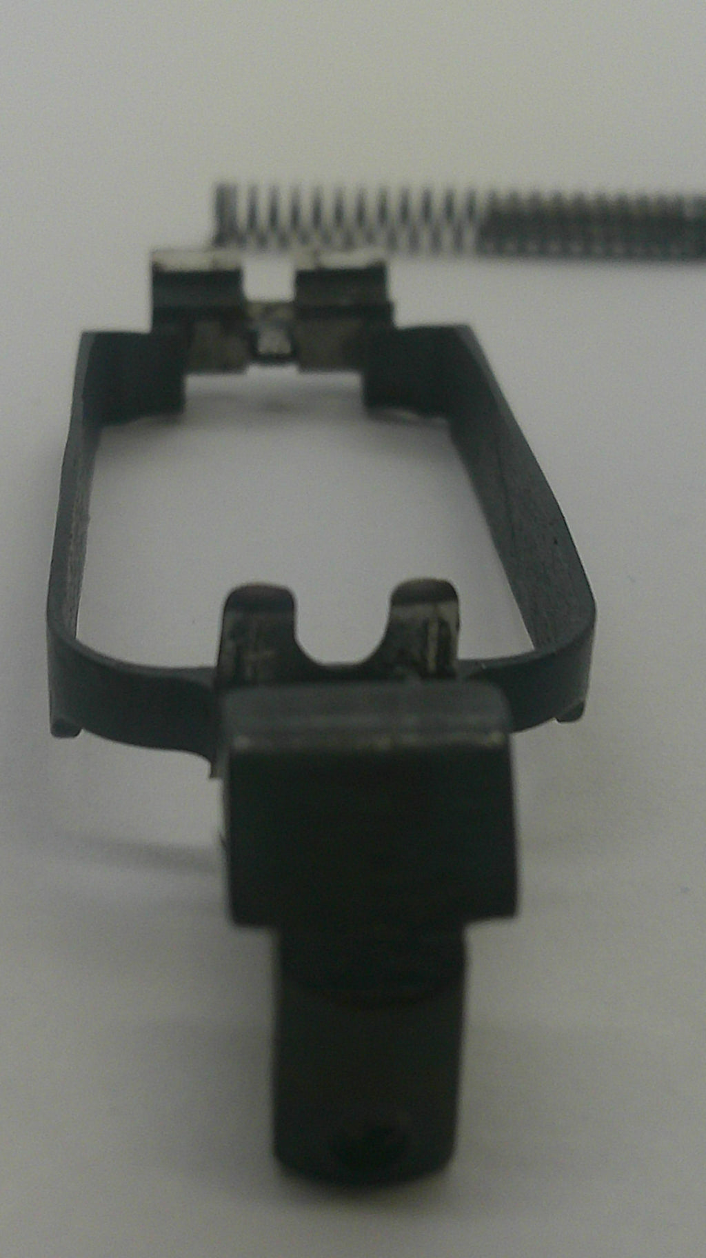A close-up of a black plastic replacement part, possibly a clip or bracket, shown next to a metal spring on a plain light background.