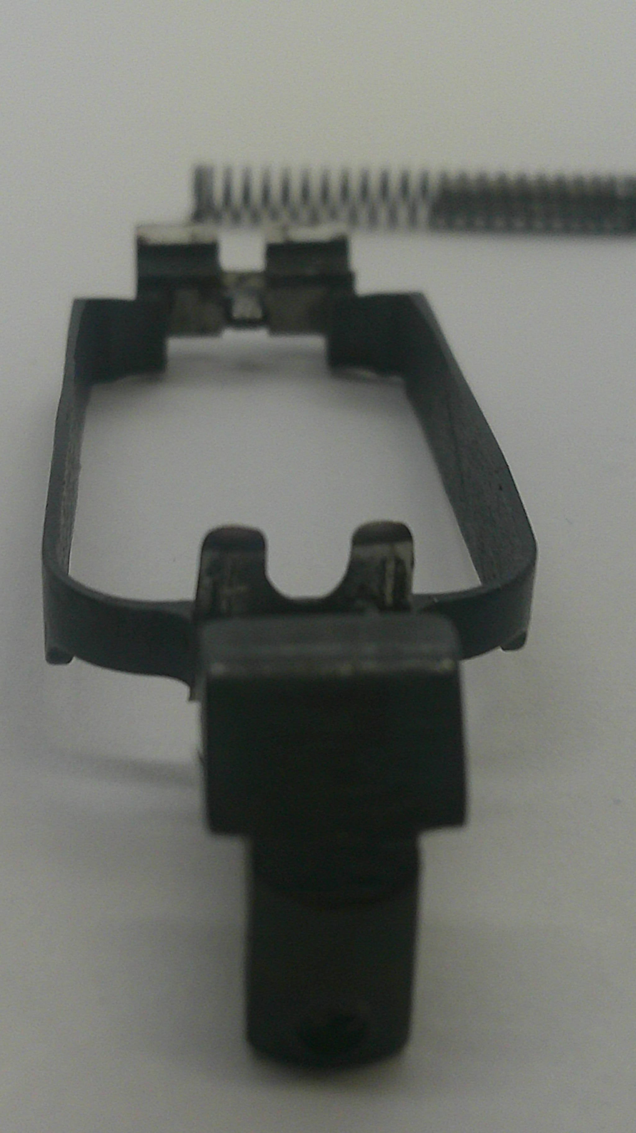A close-up of a black plastic replacement part, possibly a clip or bracket, shown next to a metal spring on a plain light background.