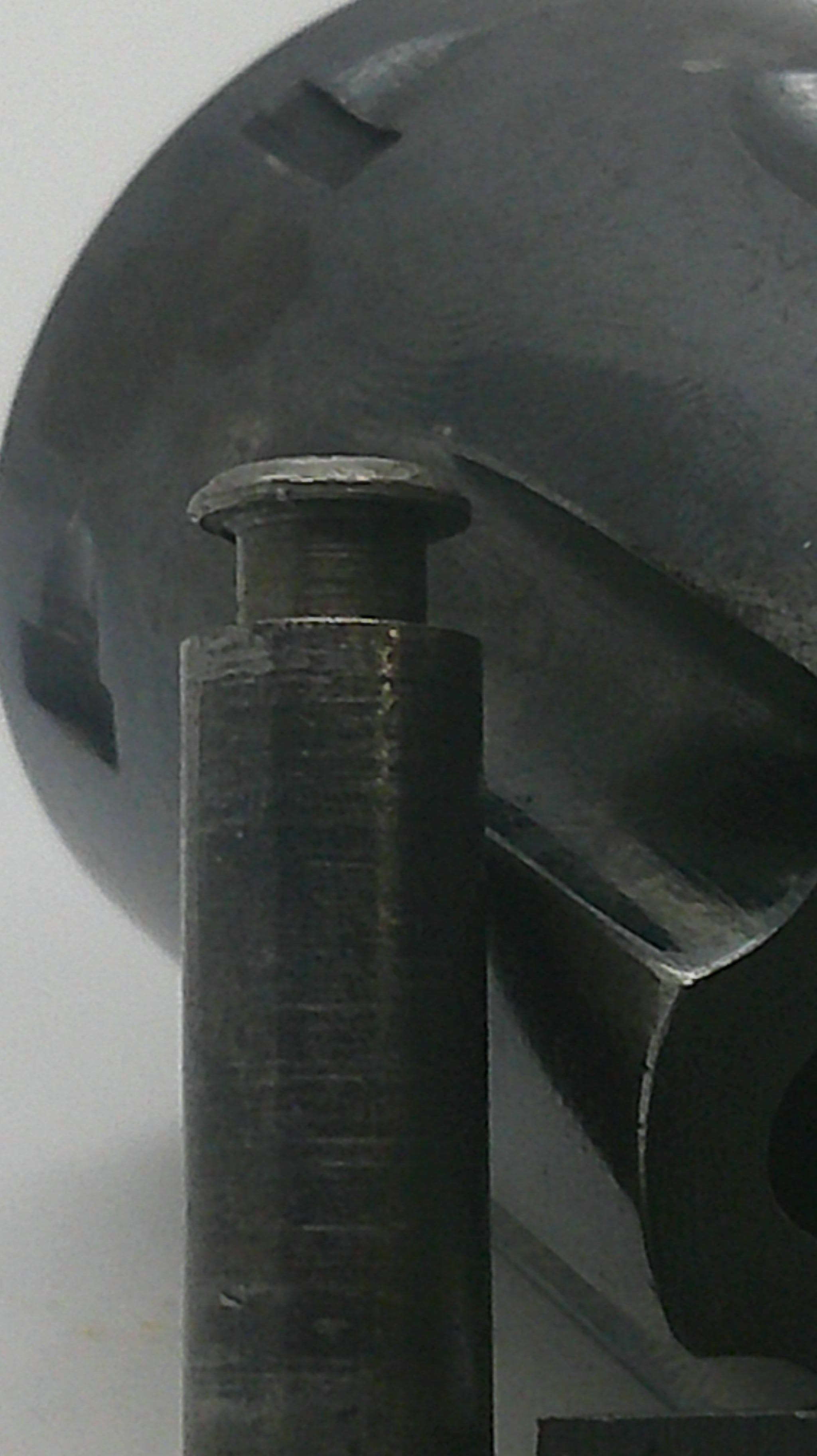 A close-up of a dark metallic cylindrical component with a threaded pin or bolt protruding from one end, set against a dark gray industrial background.