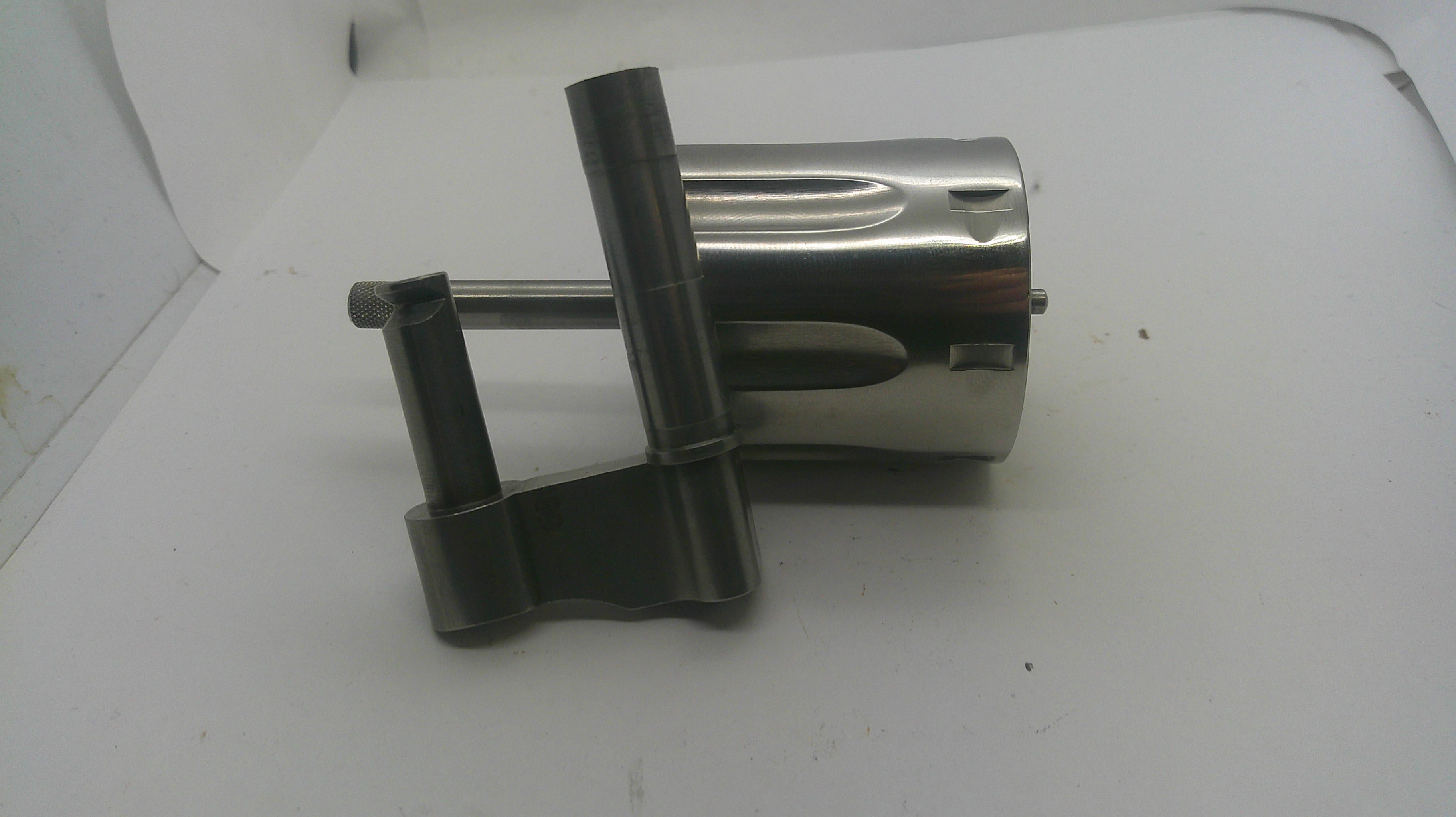 A metallic mechanical part, possibly a motor or engine component, featuring a shiny silver cylindrical body and dark gray mounting brackets, resting on a white surface.