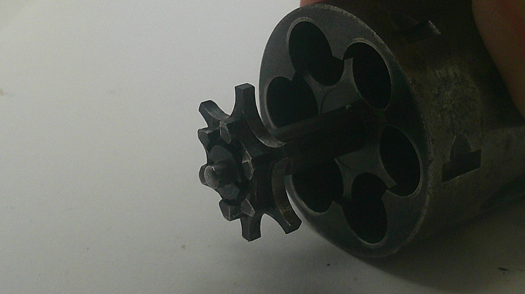 A close-up of a dark metallic revolver cylinder with a six-round chamber and a visible hand holding it on the right side against a plain light background.
