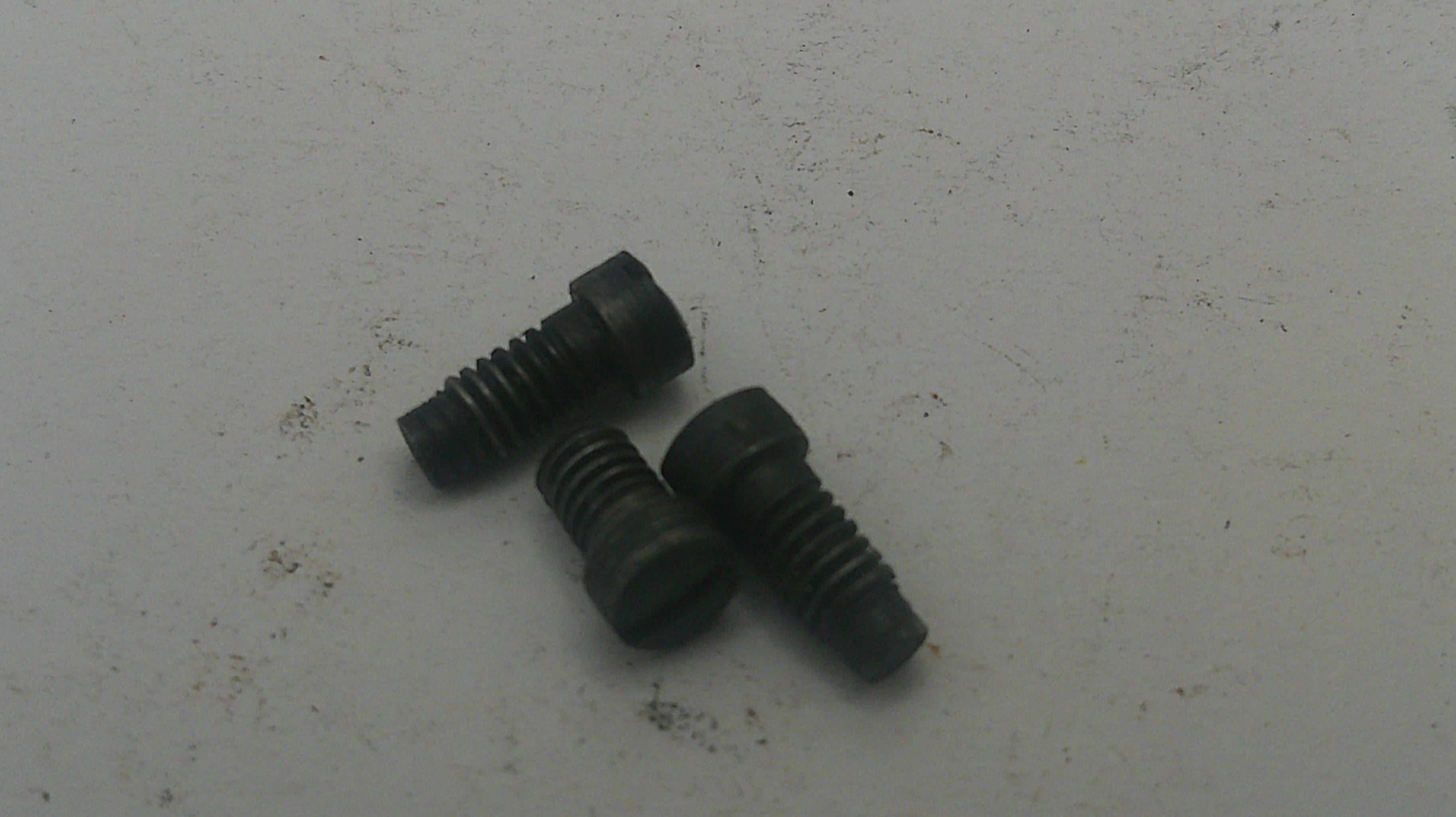 Three black screws on a white surface with visible dirt.