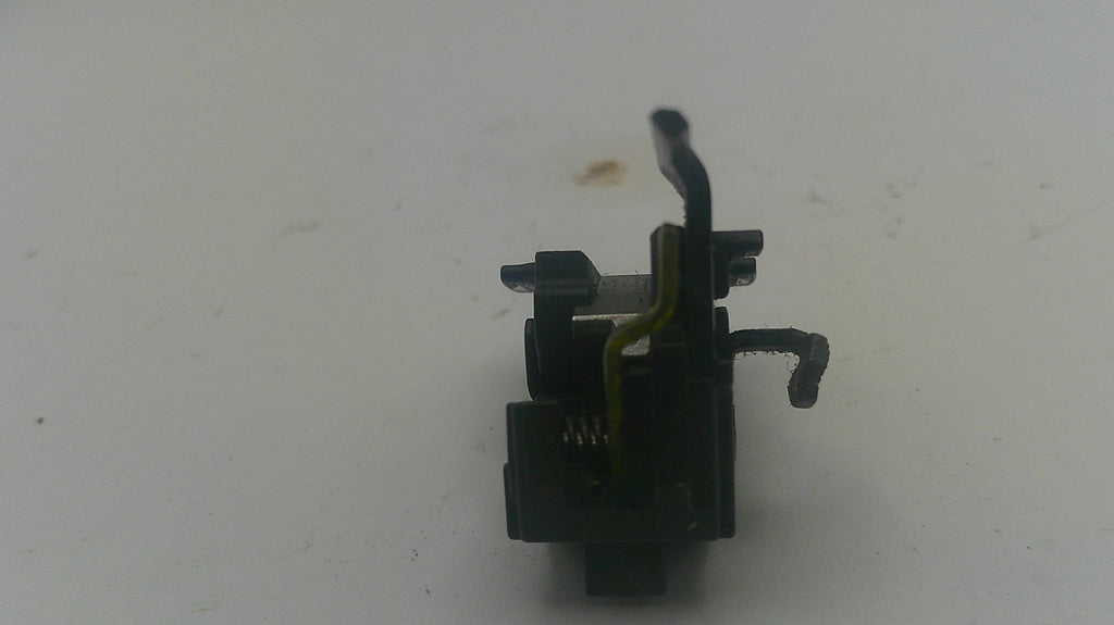 A small black plastic and metal mechanical component with a yellow wire, photographed on a plain off-white background.