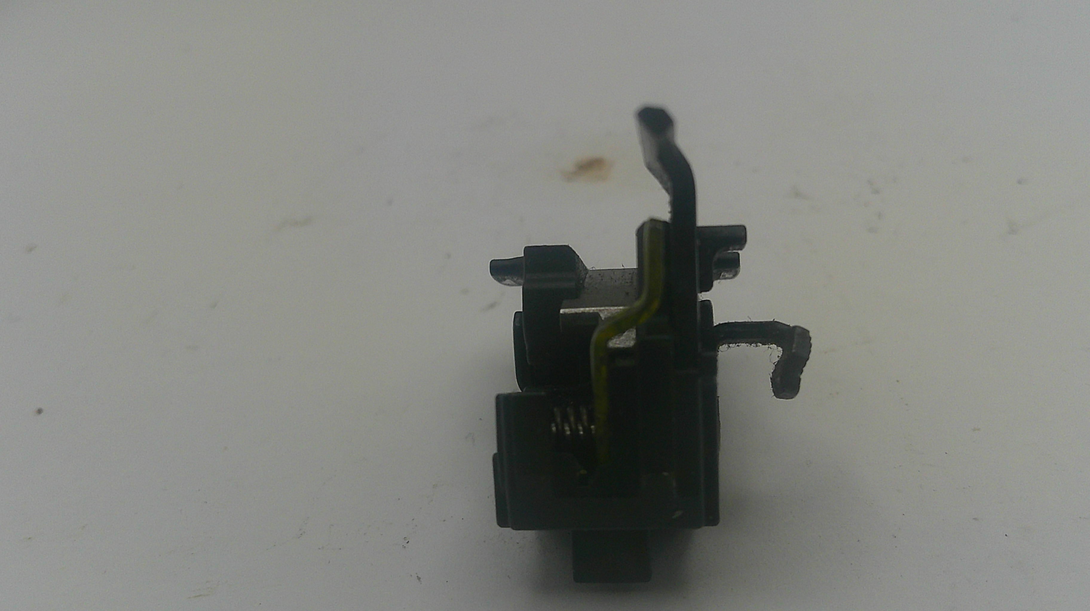 A small black plastic and metal mechanical component with a yellow wire, photographed on a plain off-white background.