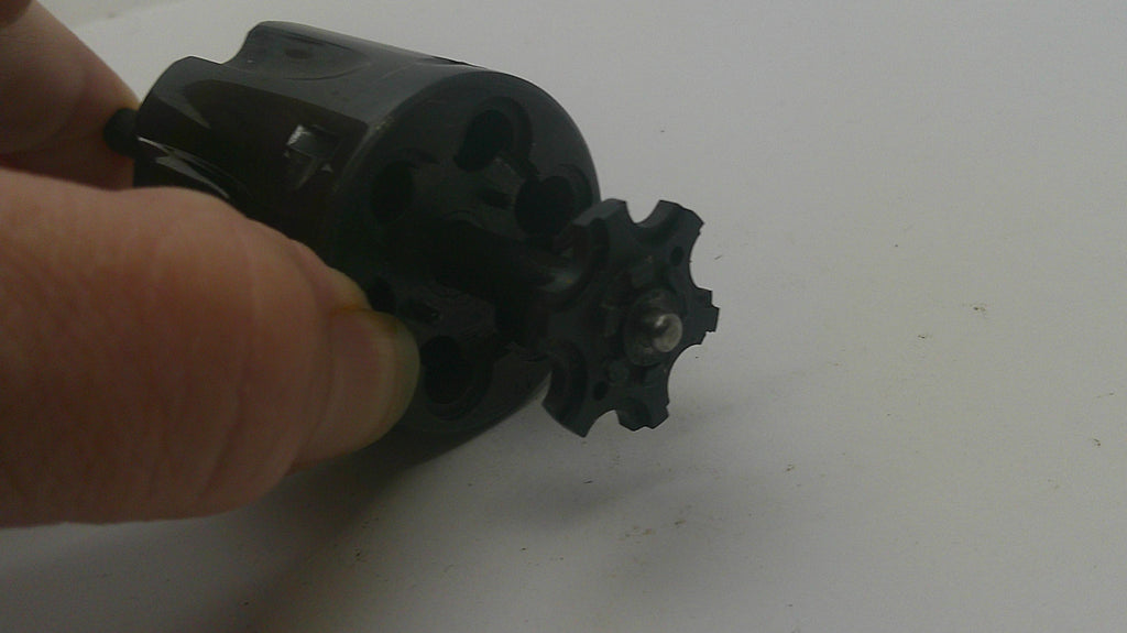 A close-up of a hand holding a black plastic revolver cylinder and internal gear mechanism against a plain light background.