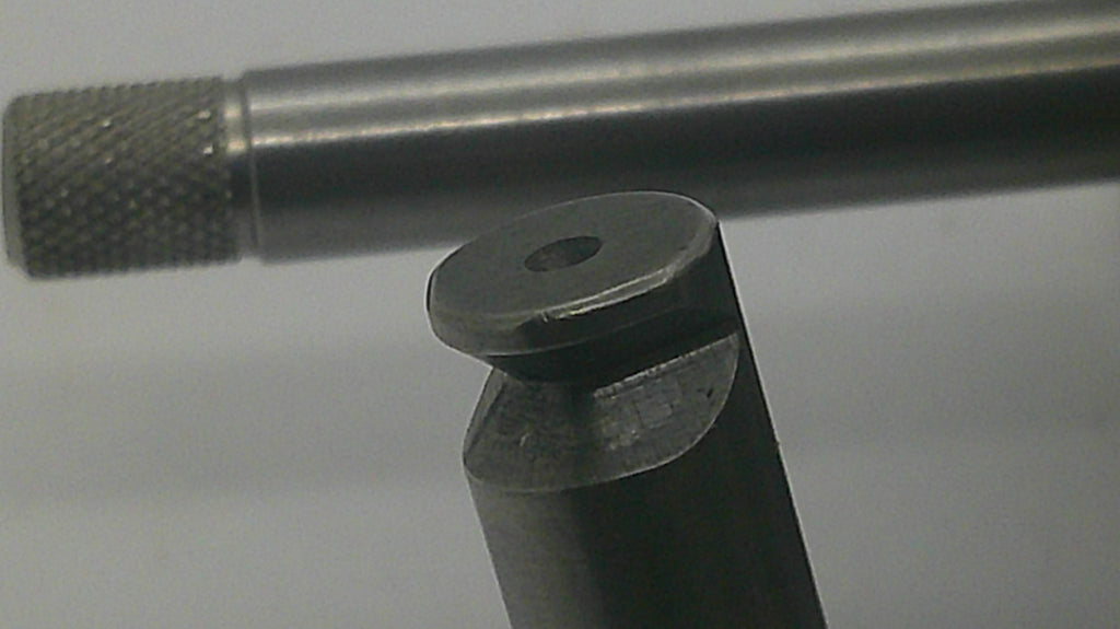 Close-up of a dark metallic cylindrical tool or hardware piece with a knurled textured end, shown against a plain light background.