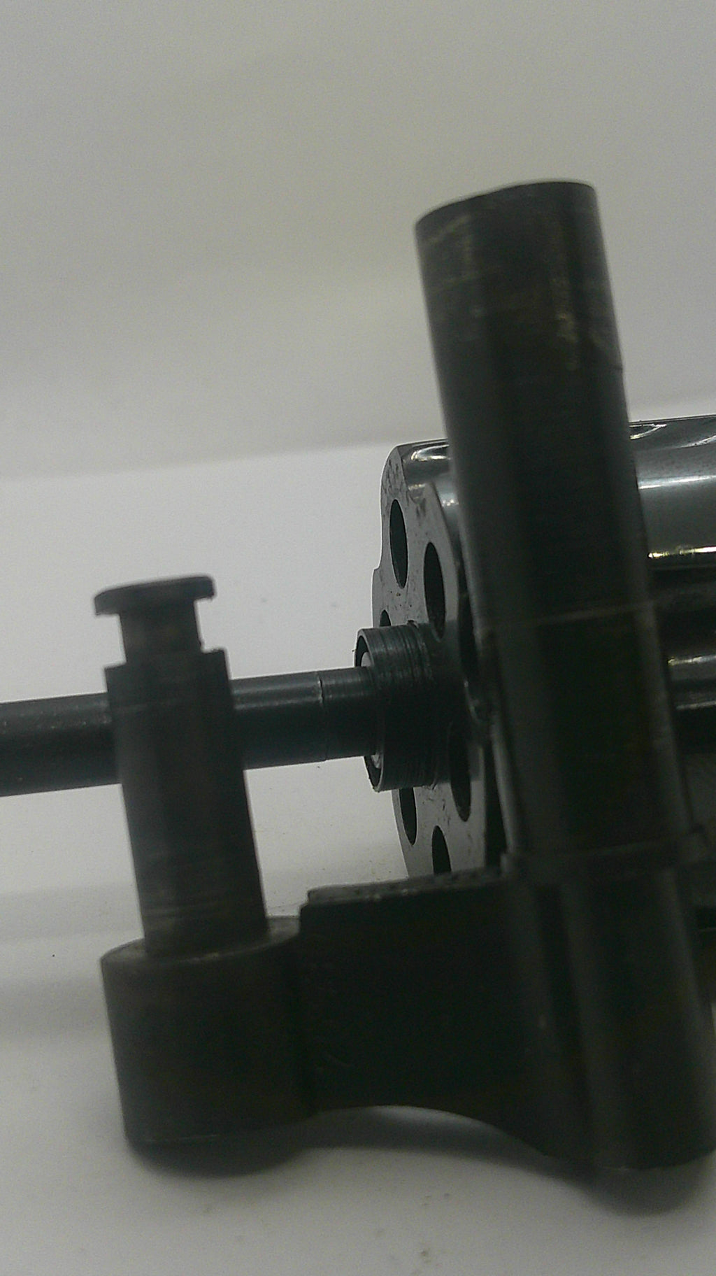 A close-up of a black metal mechanical component or tool part with cylindrical rods and circular openings, photographed against a plain light background.